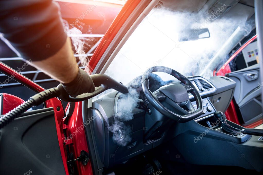 Car service worker cleans interiror with steam cleaner