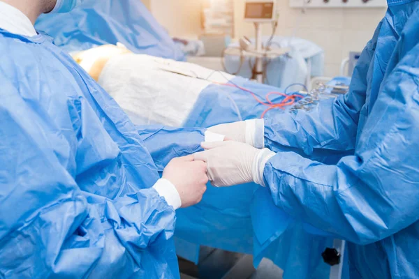 Asistente ayuda al cirujano a ponerse guantes de látex y bata quirúrgica antes de la operación. — Foto de Stock