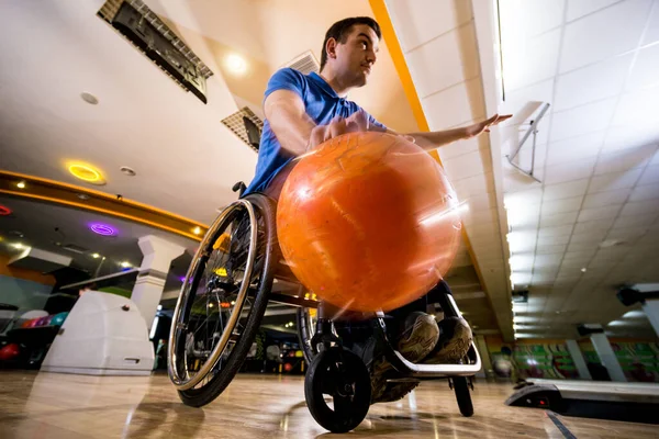 Mladý zdravotně postižený muž na invalidním vozíku hraje bowling v klubu — Stock fotografie