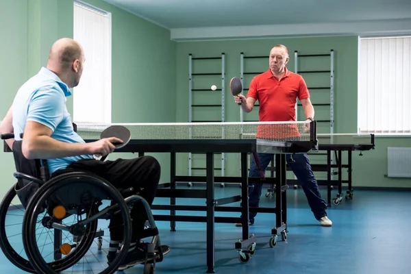 Behinderter Mann im Rollstuhl spielt mit seinem Trainer Tischtennis — Stockfoto