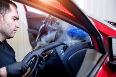 Araba servisi çalışanı iç mekanı buharlı temizleyiciyle temizliyor.