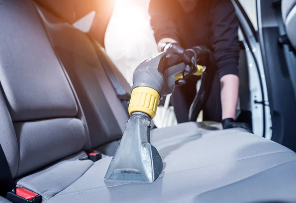 Worker cleans car interior with vacuum cleaner