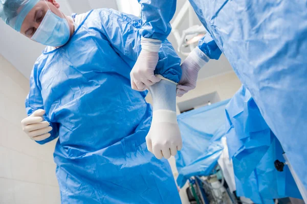 Assistant helps the surgeon put on latex gloves and surgical gown before the operation.