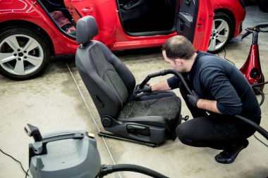 Araba servisi çalışanı elektrikli süpürgeyle araba koltuğunu temizliyor..