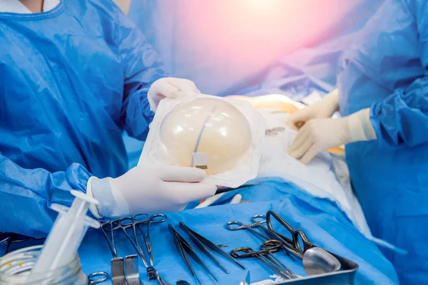 Cirurgião em sala de operação está segurando implante de silicone estéril mama nas mãos. — Fotografia de Stock