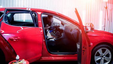 Araba servisi çalışanı iç mekanı buharlı temizleyiciyle temizliyor.