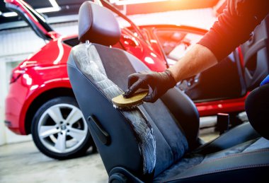 Araba servisi çalışanı araba koltuğunu özel bir fırçayla temizliyor.