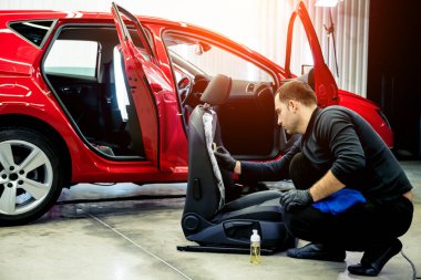 Araba servisi çalışanı araba koltuğunu özel bir fırçayla temizliyor.