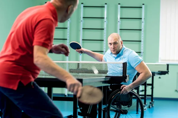 Дорослий інвалідний чоловік у візку грає на настільному тенісі зі своїм тренером — стокове фото