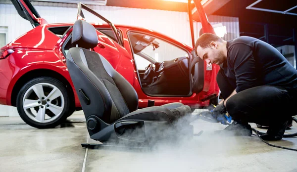 Trabajador de servicio de coches limpiando asiento de coche con un limpiador de vapor — Foto de Stock