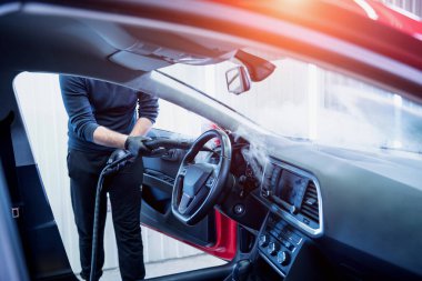 Araba servisi çalışanı iç mekanı buharlı temizleyiciyle temizliyor.