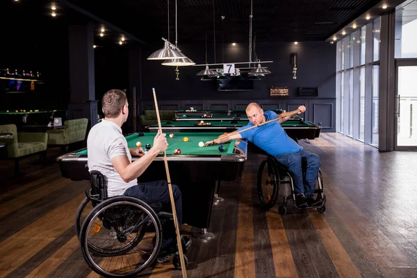 Adult men with disabilities in a wheelchair play billiards in the club