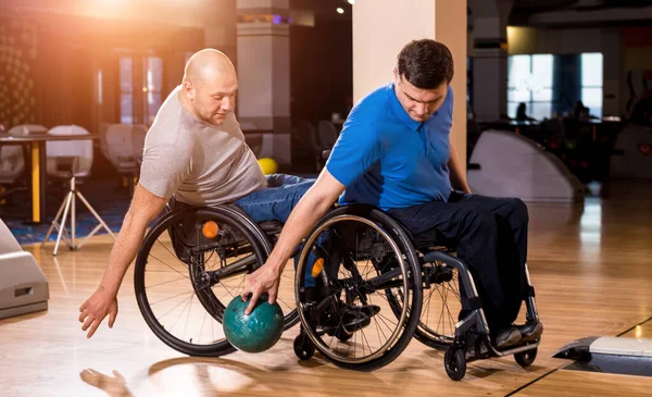 Two young disabled men in wheelchairs playing bowling in the club — Stock Photo, Image