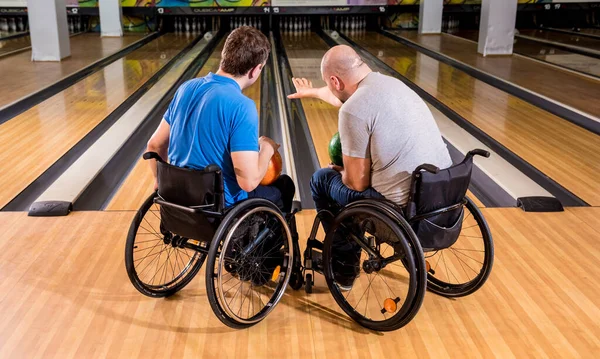 Dos jóvenes discapacitados en sillas de ruedas jugando bolos en el club —  Fotos de Stock