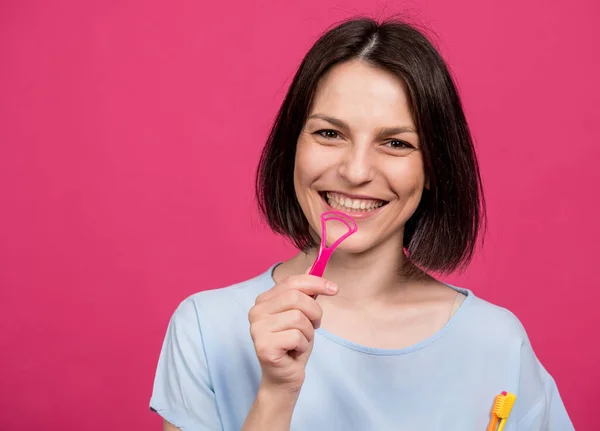 Schöne glückliche junge Frau mit Zungenschaber auf leerem rosa Hintergrund — Stockfoto