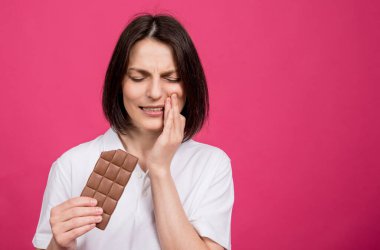 Güzel genç bir kadın bir çikolata çubuğunu ısırır ve dişi ağrır.