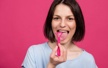 Güzel, mutlu, pembe arka planda dil kazıyıcısı olan genç bir kadın.