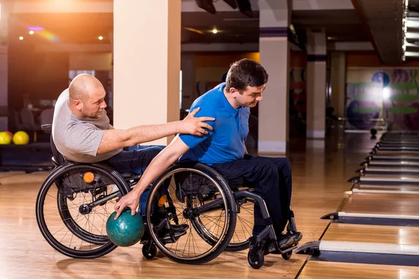 Two young disabled men in wheelchairs playing bowling in the club — Stock Photo, Image