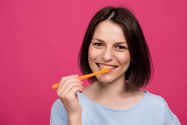 Güzel, mutlu, pembe arka planda diş fırçası olan genç bir kadın.