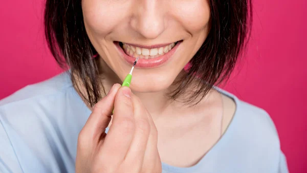 Schöne glückliche junge Frau mit Interdentalbürste auf rosa Hintergrund — Stockfoto