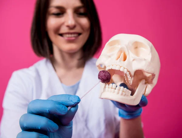 Beautiful girl proposes lollipop for artificial skull — Stock Photo, Image