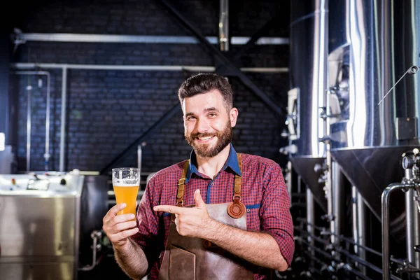 A bőrkötényt viselő fiatal sörfőző sört tesztel egy modern sörfőzdében. — Stock Fotó