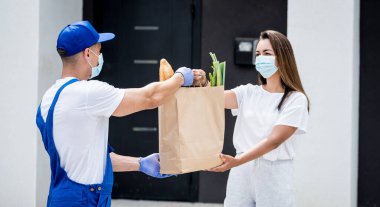 Koruyucu maske takan ve eldiven takan genç bir kurye karantina sırasında genç bir kadına mal teslim ediyor.