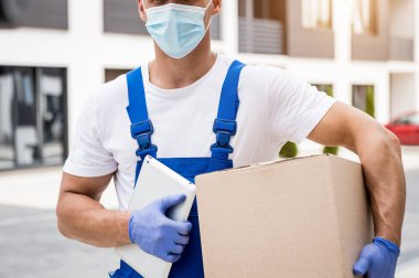 Koruyucu maske takan ve eldiven takan genç kurye karantina sırasında mal teslim ediyor.