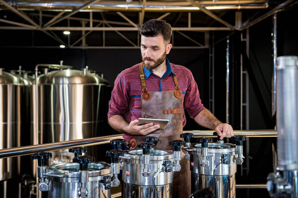 Молодой пивовар в кожаном фартуке контролирует процесс брожения пива на современном пивоваренном заводе