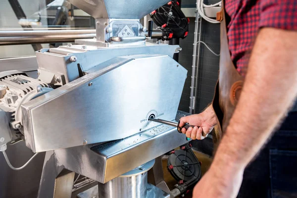 Een jonge brouwer in een leren schort controleert het malen van moutzaden in een molen in een moderne brouwerij — Stockfoto