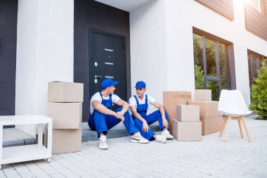 İki nakliye şirketi çalışanı merdivende otururken mola veriyor.