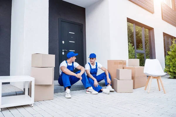 İki nakliye şirketi çalışanı merdivende otururken mola veriyor.