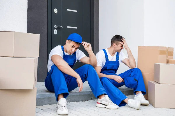 İki nakliye şirketi çalışanı merdivende otururken mola veriyor.