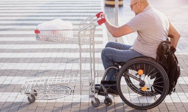 Tekerlekli sandalyedeki engelli adam süpermarketin önünde arabasını itiyor.