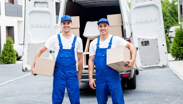 Zwei Mitarbeiter einer Umzugsfirma entladen Kisten aus Kleinbus in die Wohnung der Kunden — Stockfoto