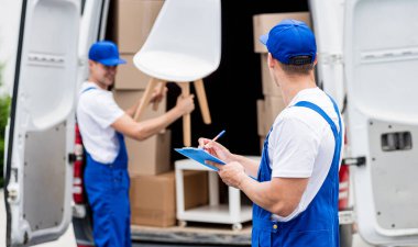 İki nakliye şirketi çalışanı minibüsten yeni eve kutular boşaltıyor.