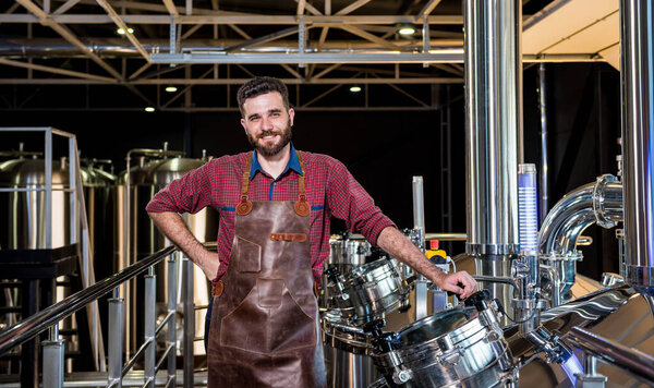 Молодой пивовар в кожаном фартуке контролирует процесс брожения пива на современном пивоваренном заводе