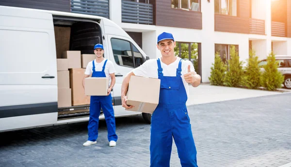 Dos trabajadores de la empresa de mudanzas descargan cajas de minibús en un nuevo hogar — Foto de Stock