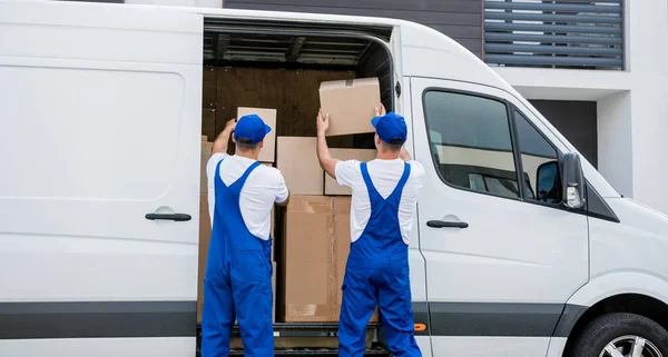 Два працівники компаній з вивезення розвантажують коробки з мікроавтобуса в новий будинок — стокове фото