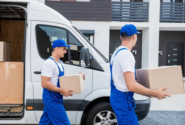 Zwei Mitarbeiter einer Umzugsfirma laden Kisten aus Kleinbus in neues Zuhause — Stockfoto