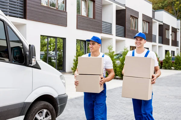 Zwei Mitarbeiter einer Umzugsfirma laden Kisten aus Kleinbus in neues Zuhause — Stockfoto