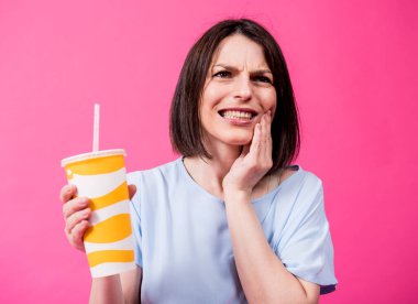 Hassas dişleri olan genç kadın arka planda soğuk su içiyor.