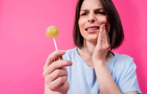 Junge Frau mit empfindlichen Zähnen isst süßen Lutscher auf farbigem Hintergrund — Stockfoto