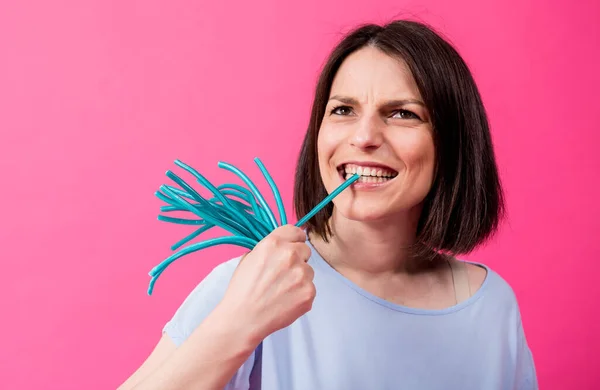 Junge Frau mit empfindlichen Zähnen isst süße Bonbons auf farbigem Hintergrund — Stockfoto