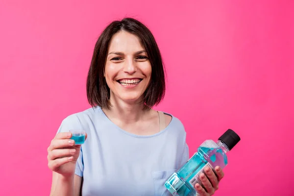 Mooi meisje maakt gebruik van mondwater op de roze achtergrond — Stockfoto