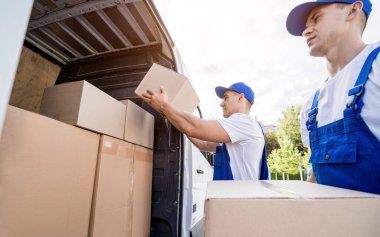 İki nakliye şirketi çalışanı minibüsten kutuları boşaltıyor.