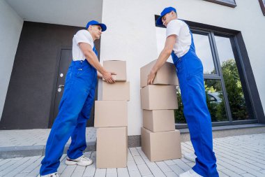 İki nakliye şirketi çalışanı minibüsten müşterilerin evlerine kutu indiriyor.