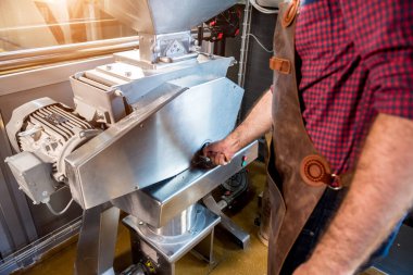 Deri önlüklü genç bir bira üreticisi modern bir bira fabrikasında malt tohumlarının öğütülmesini kontrol eder.