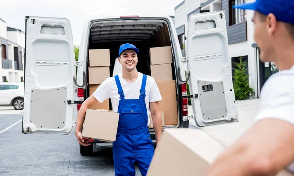 Zwei Mitarbeiter einer Umzugsfirma entladen Kisten aus Kleinbus in die Wohnung der Kunden — Stockfoto