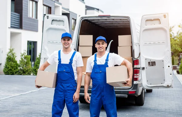 Dos trabajadores de la empresa de mudanzas descargan cajas de minibús en el hogar de los clientes —  Fotos de Stock